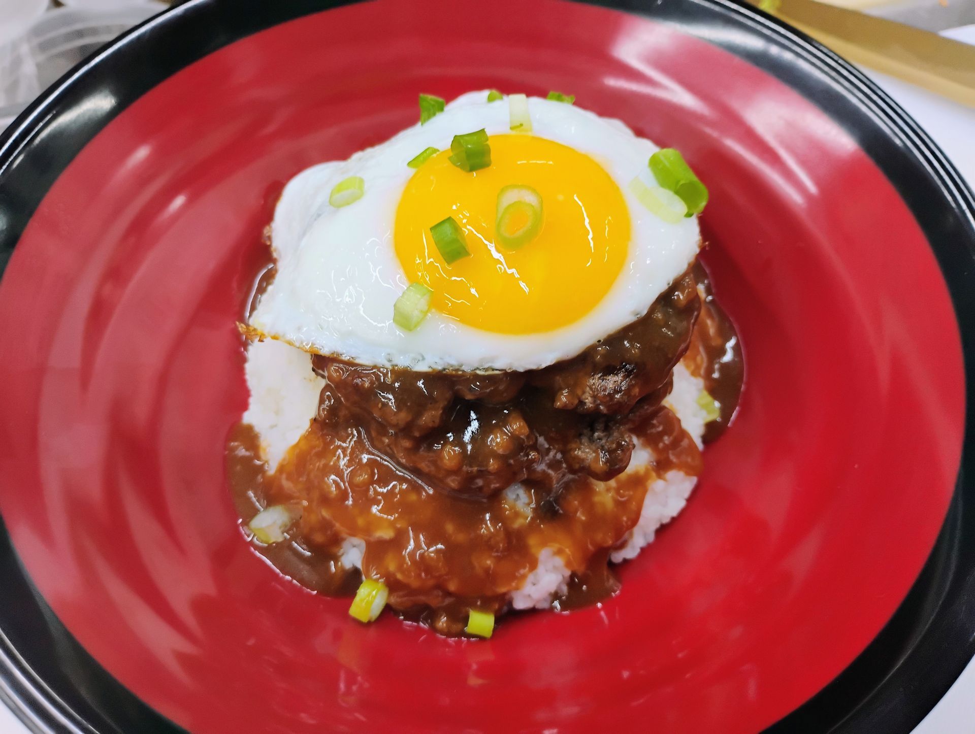 Red plate with a rice dish topped by a sunny-side-up egg and green garnish.