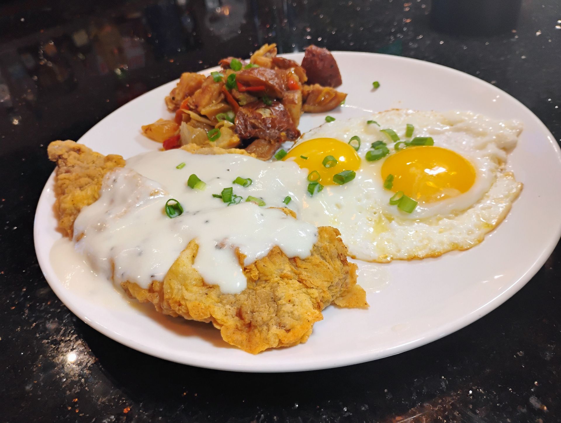 Plate with fried eggs, creamy sauce, and a side of spicy stir-fried dish on a white plate