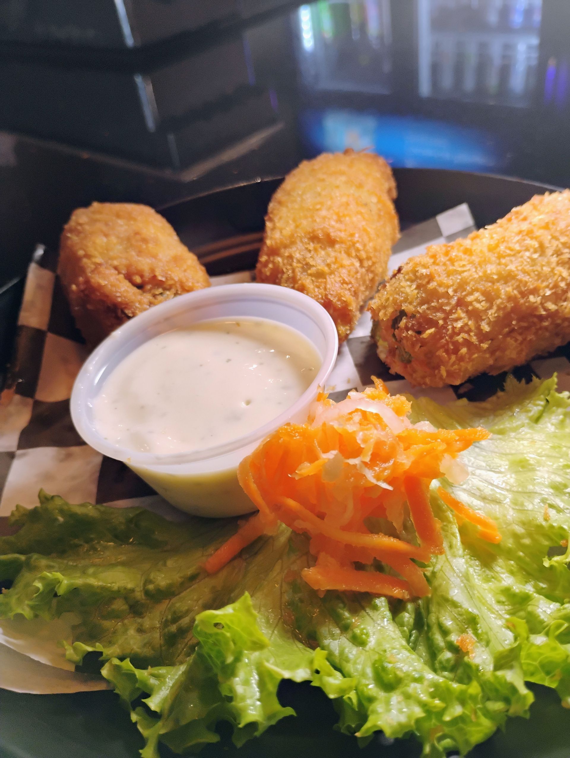 Breaded appetizers with dipping sauce on a plate, garnished with lettuce and shredded carrots