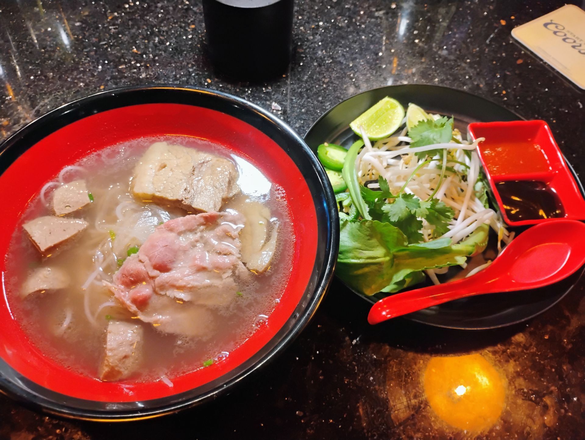 Two bowls of noodle soup, one with red broth and one with greens, on a dark table.