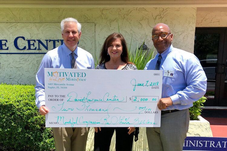 Three people holding a large check in front of a building that says motivated
