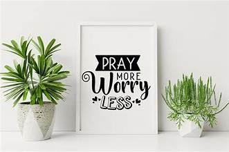 A framed poster that says `` pray more worry less '' is sitting on a table next to potted plants.