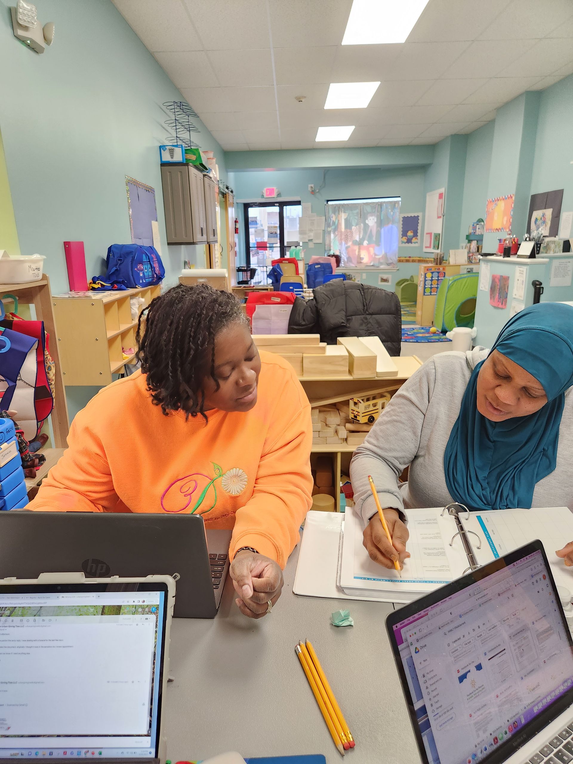 Two women are sitting at a table with laptops in a classroom.