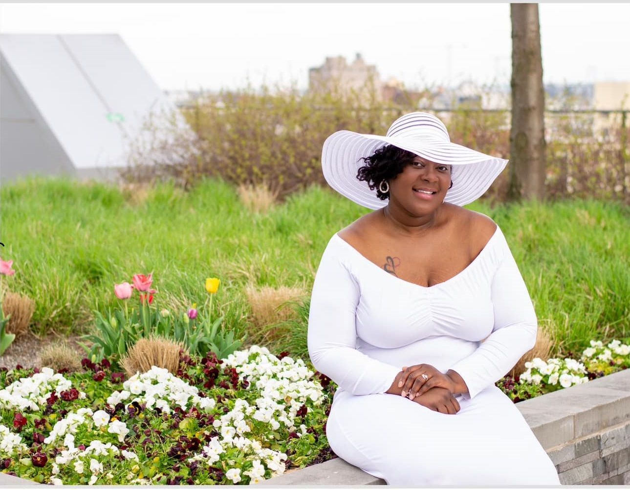 A woman in a white dress and hat is sitting in front of flowers.