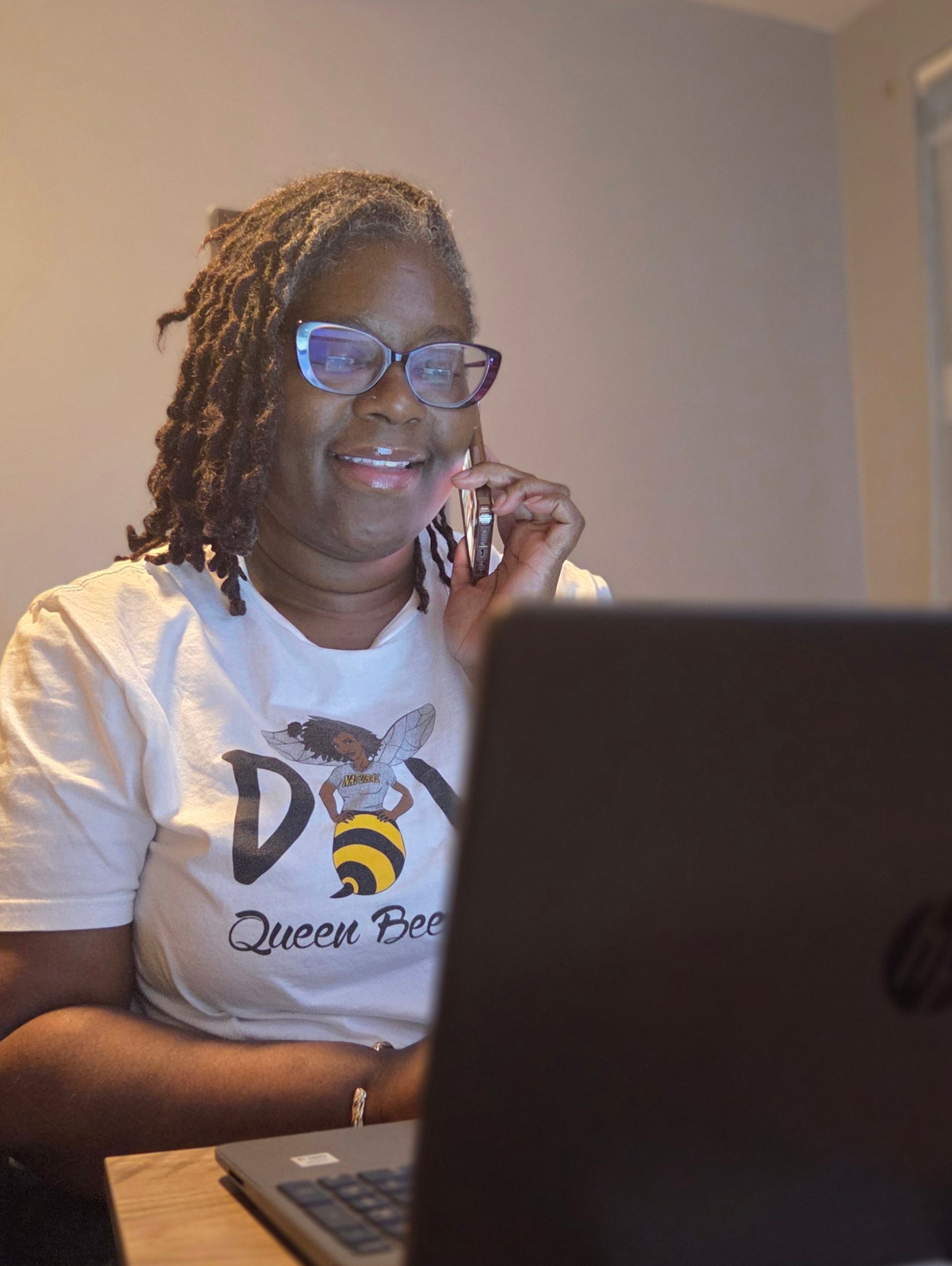A woman is sitting in front of a laptop computer talking on a cell phone.