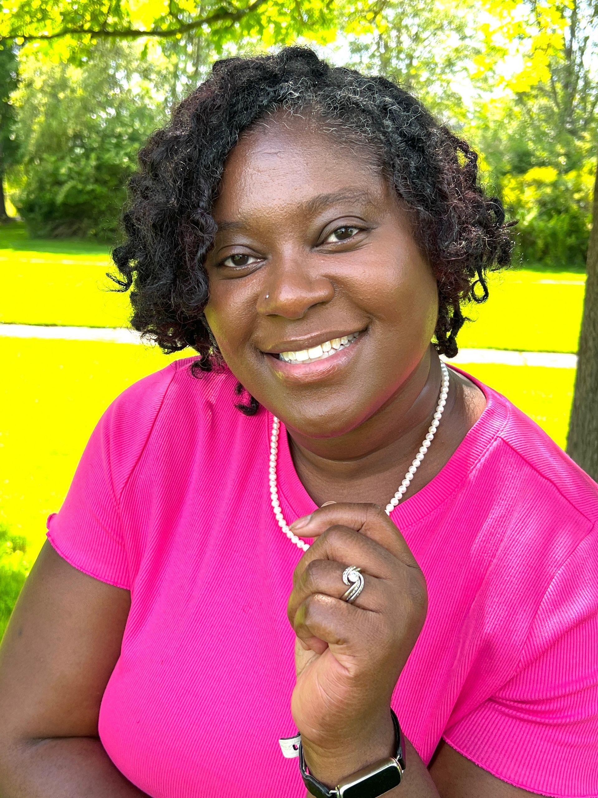 A woman in a pink shirt and pearl necklace is smiling for the camera.