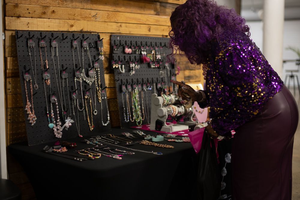 A woman with purple hair is standing in front of a table full of jewelry.