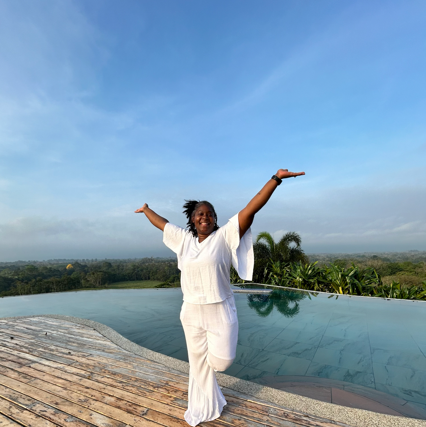 A woman is standing in front of a swimming pool with her arms outstretched.