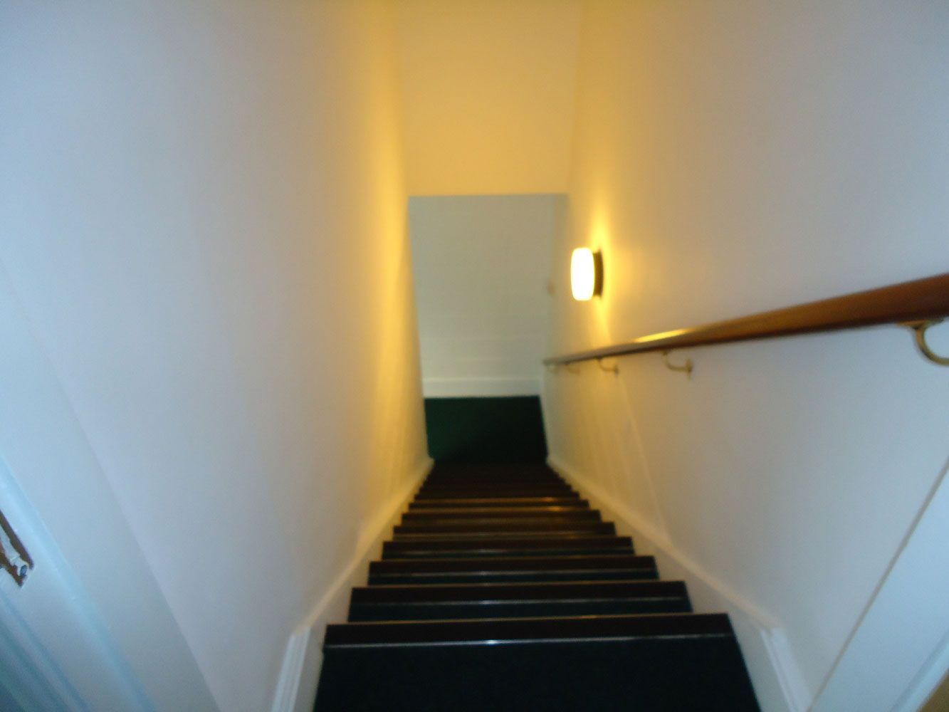 A staircase with a wooden railing and a light on the wall