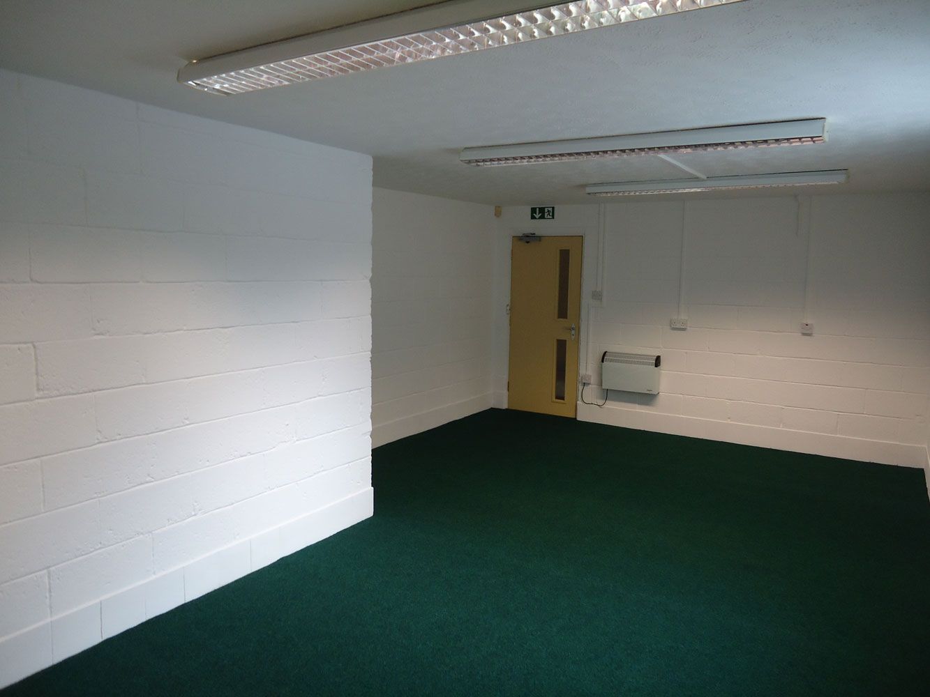 An empty room with green carpet and white brick walls