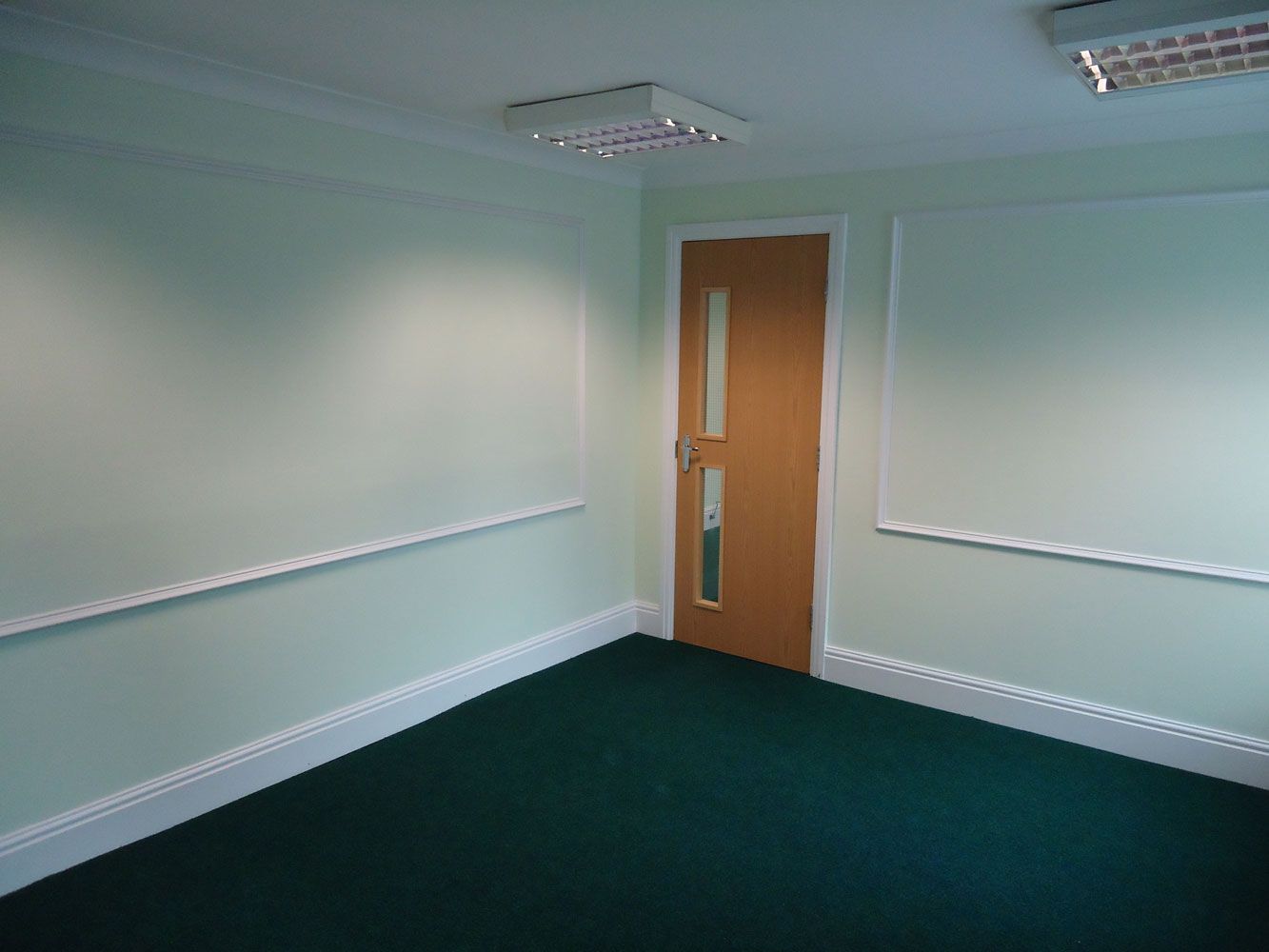 An empty room with green carpet and a door