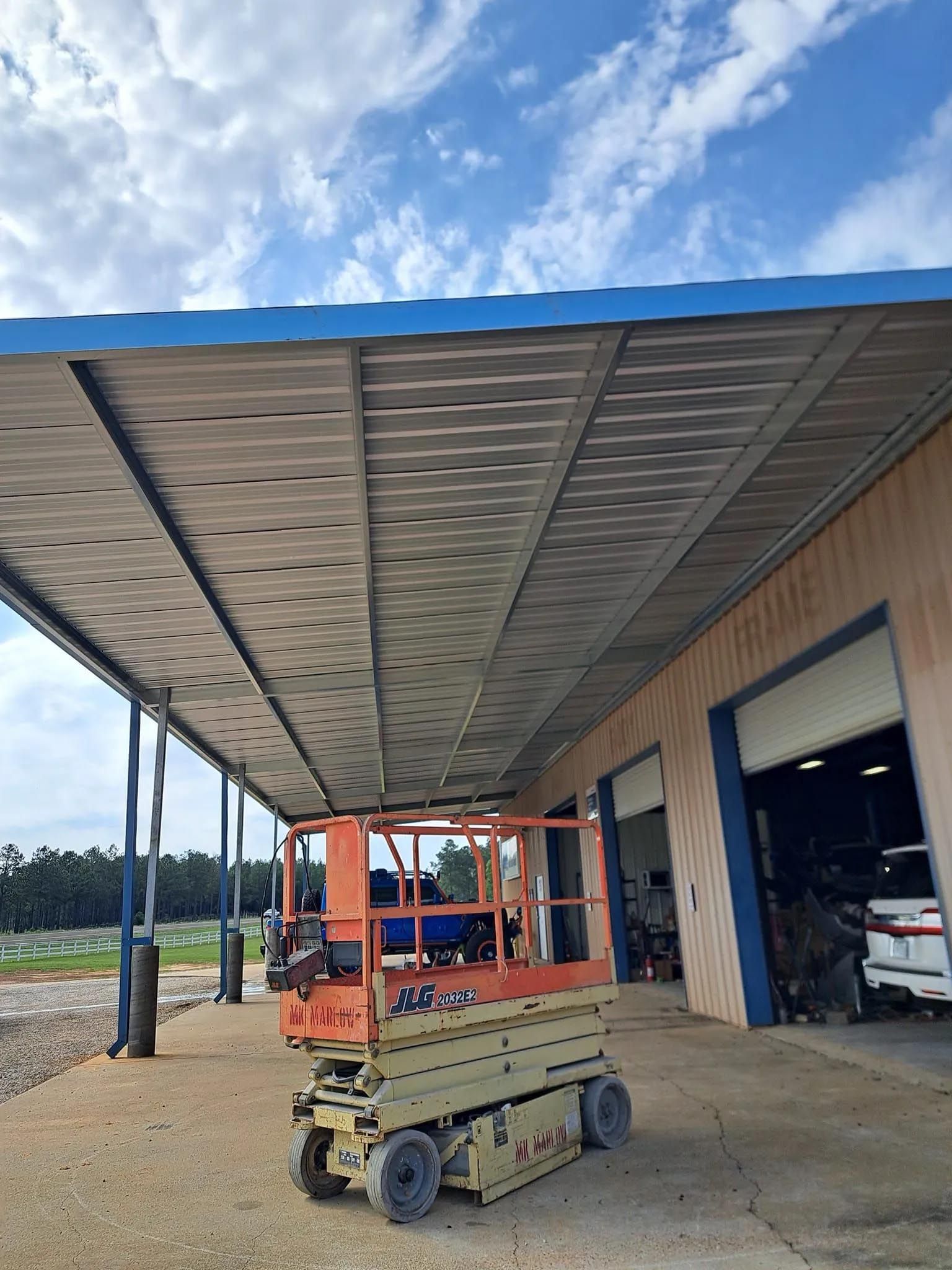 A scissor lift is parked under a canopy in front of a building.