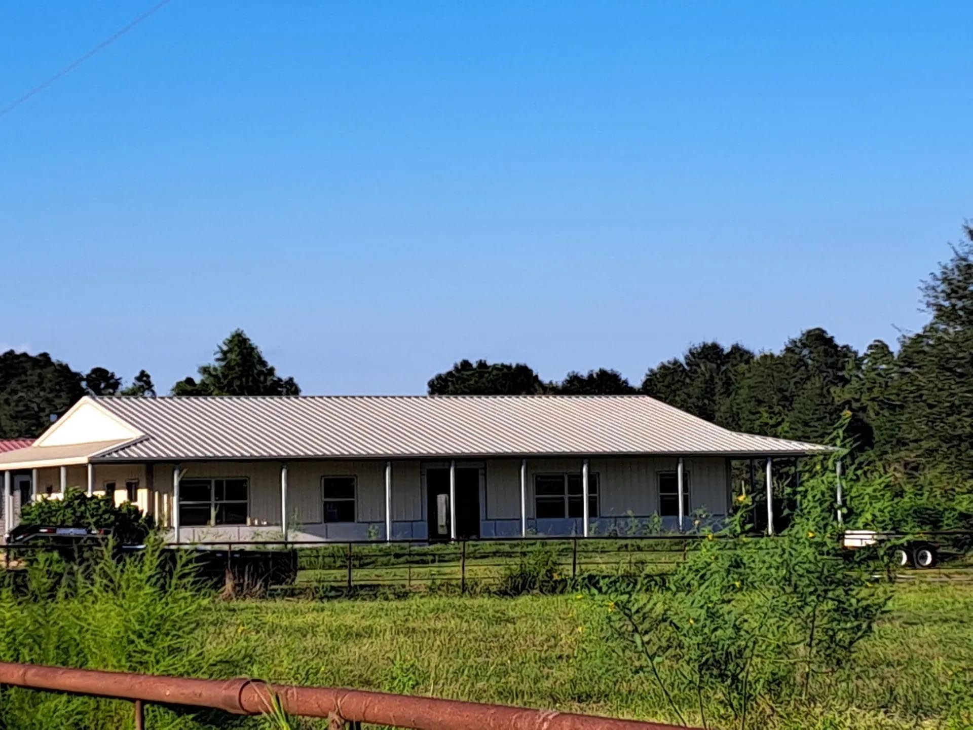 A white house with a metal roof sits in a grassy field
