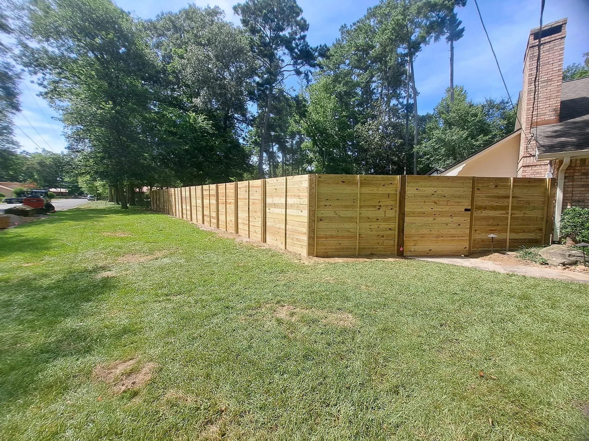 A wooden fence is in the middle of a lush green yard.