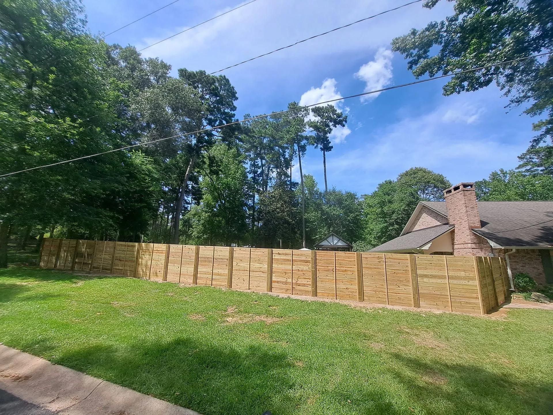 A wooden fence surrounds a lush green yard in front of a house.