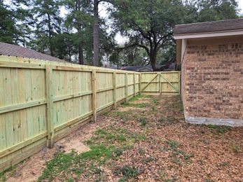 A wooden fence surrounds a brick building in a backyard.