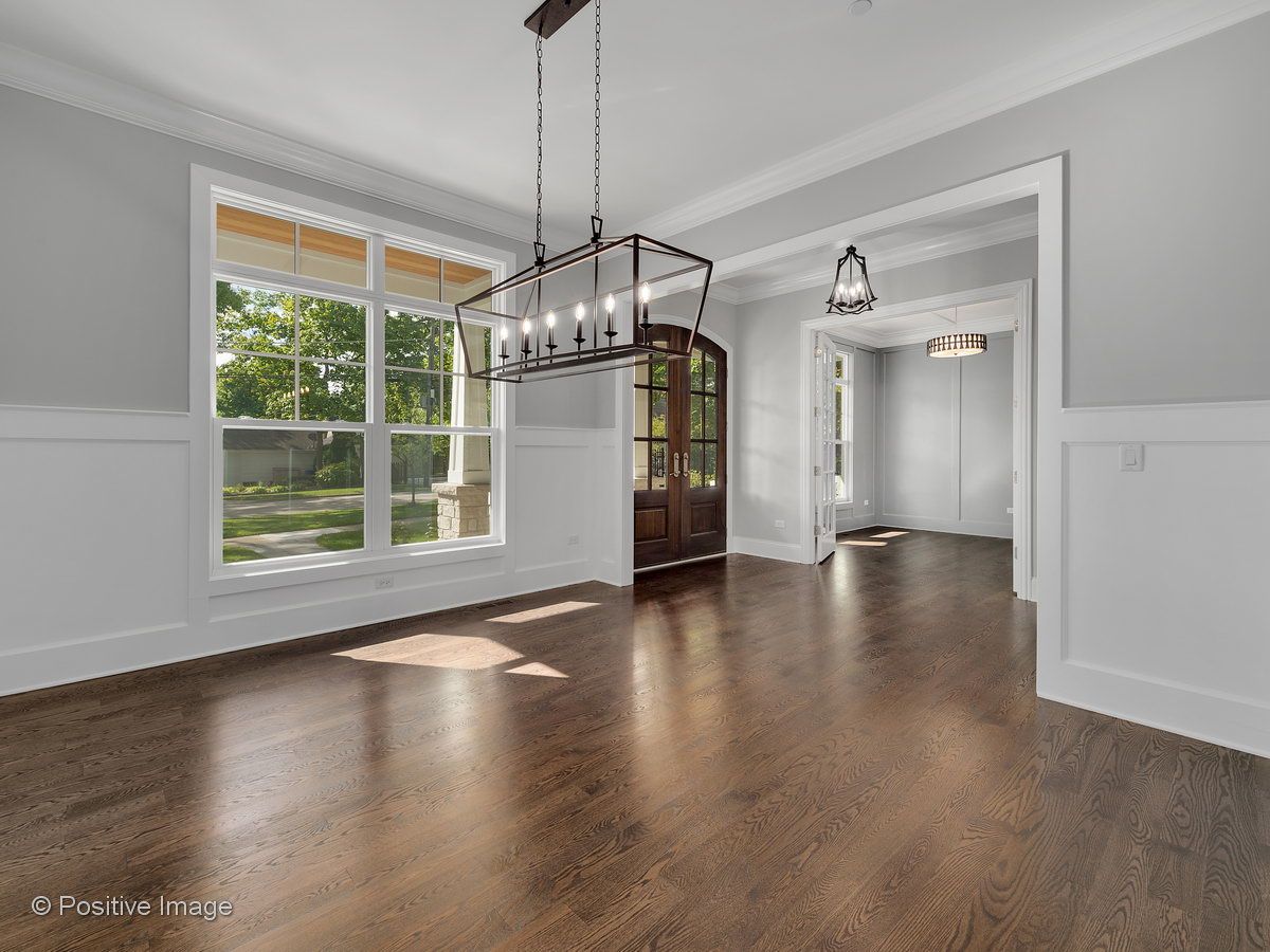 An empty dining room with hardwood floors and a chandelier hanging from the ceiling.