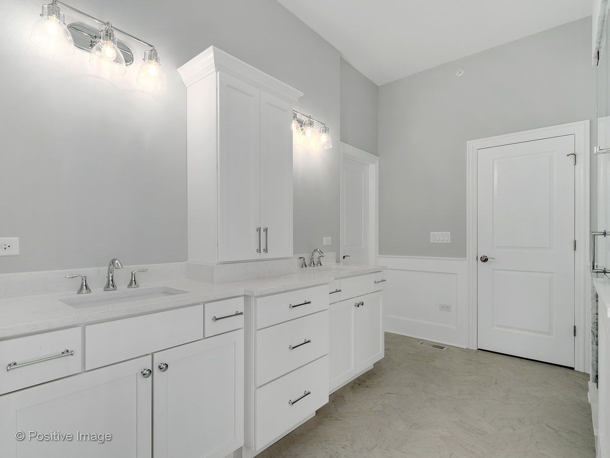 A bathroom with two sinks , two mirrors , and white cabinets.