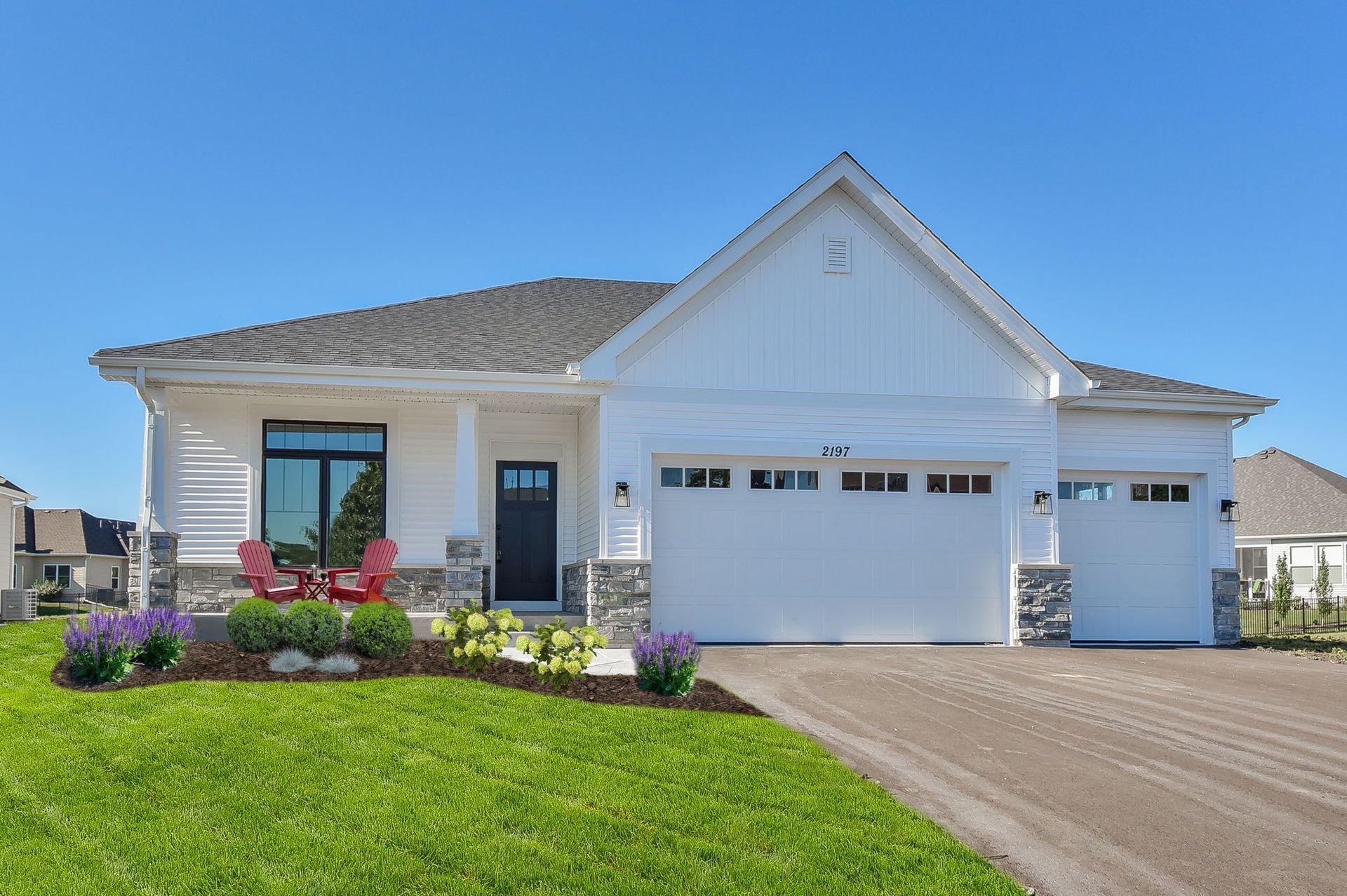 A white house with a large garage and a large lawn in front of it.