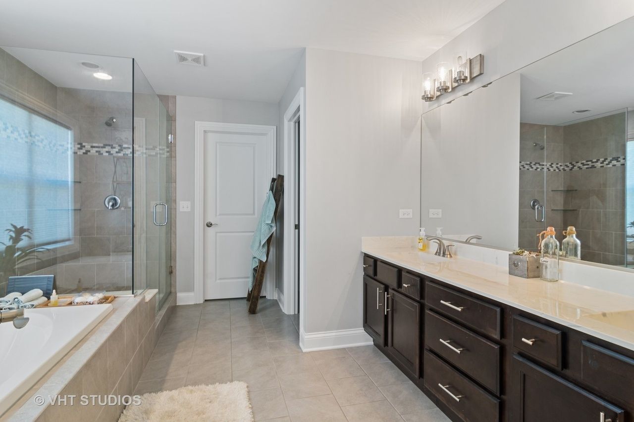 A bathroom with two sinks , a tub , and a large mirror.
