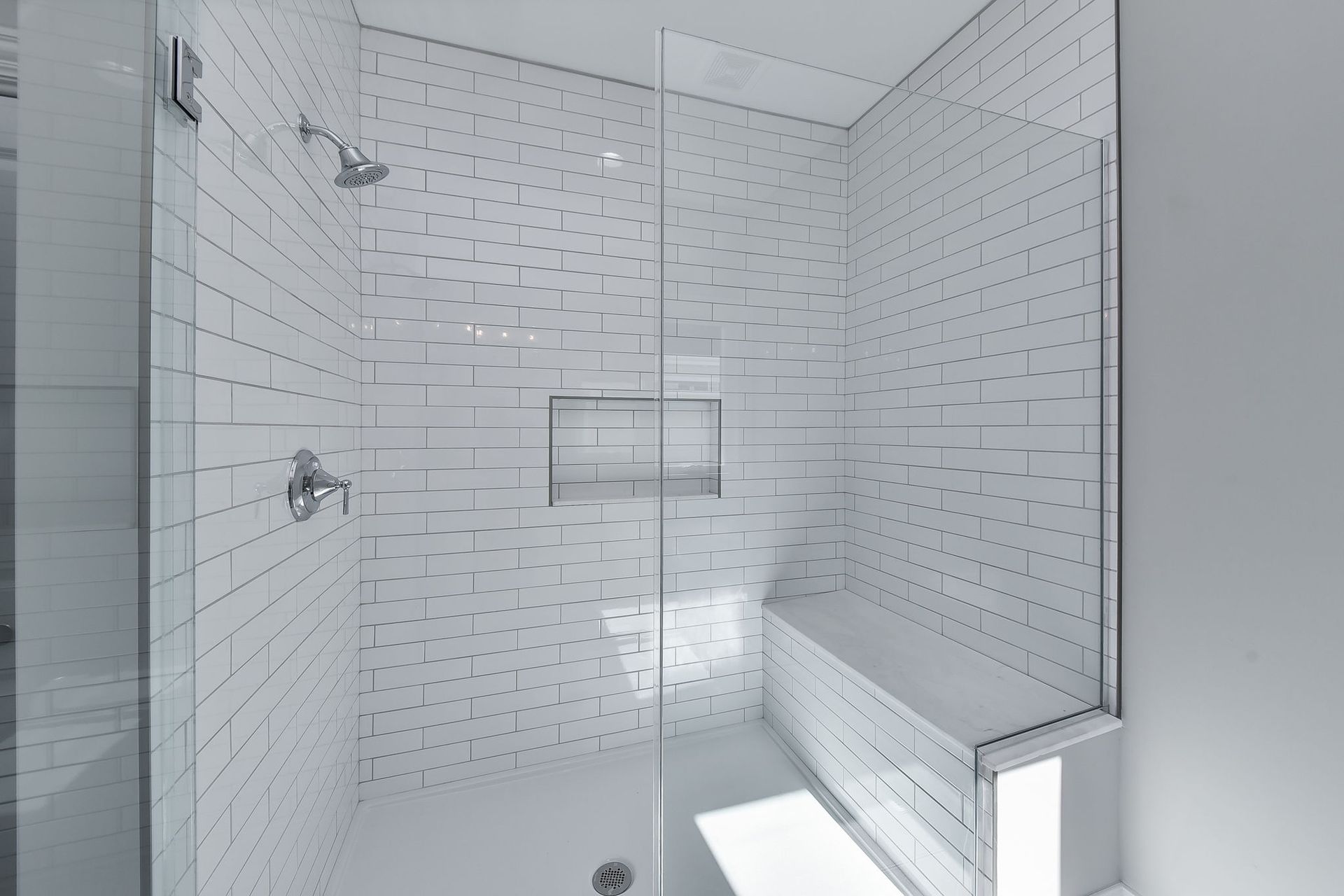 A bathroom with white tiles and a walk in shower with a glass door.