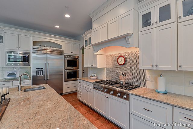 A kitchen with white cabinets , granite counter tops , stainless steel appliances and a large island.