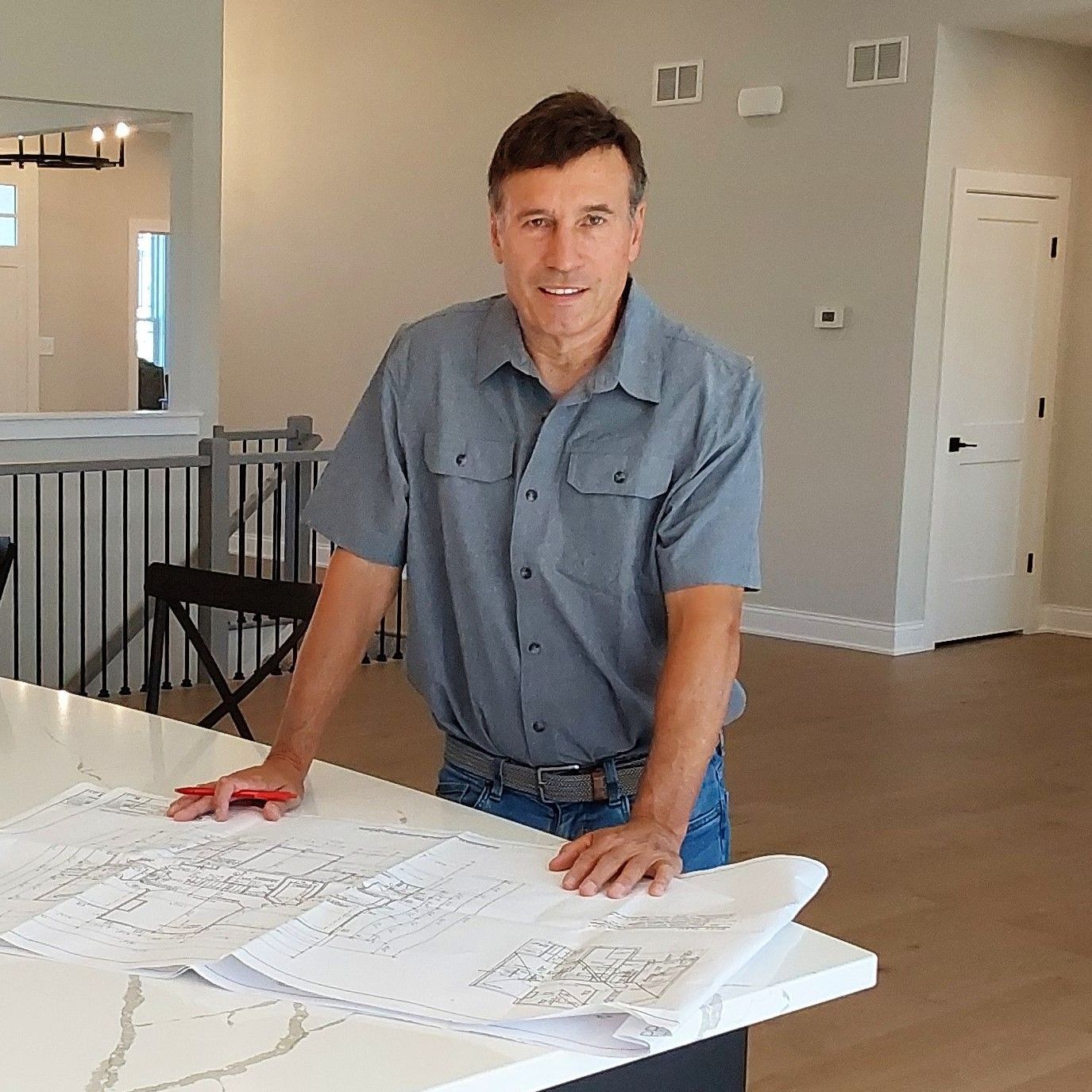 A man in a blue shirt is standing next to a table with a blueprint on it.