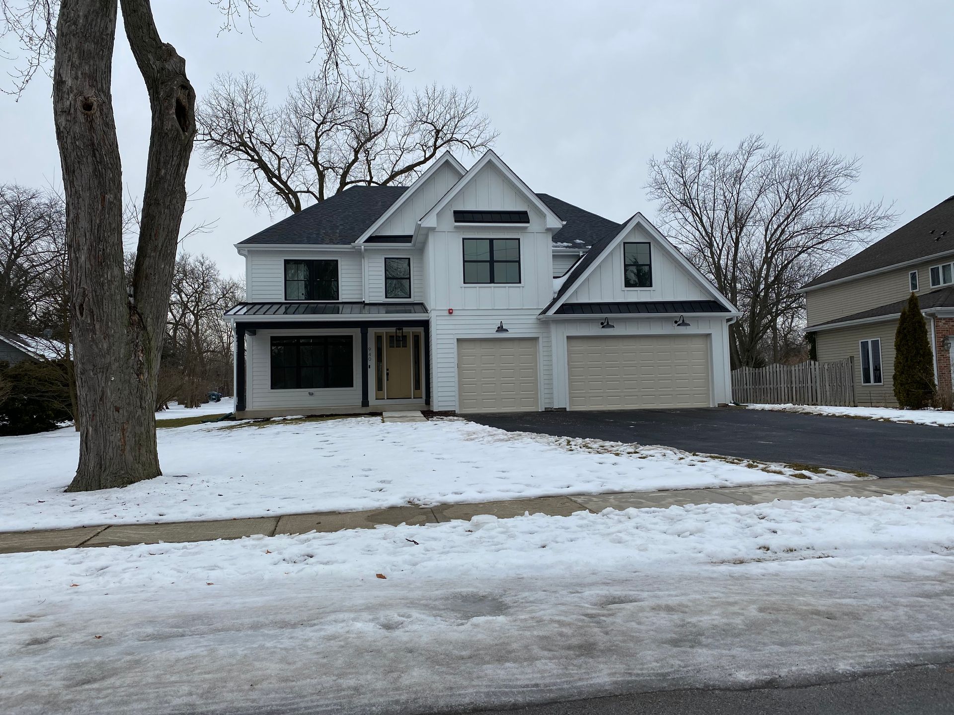 A large white house with a black roof is covered in snow.