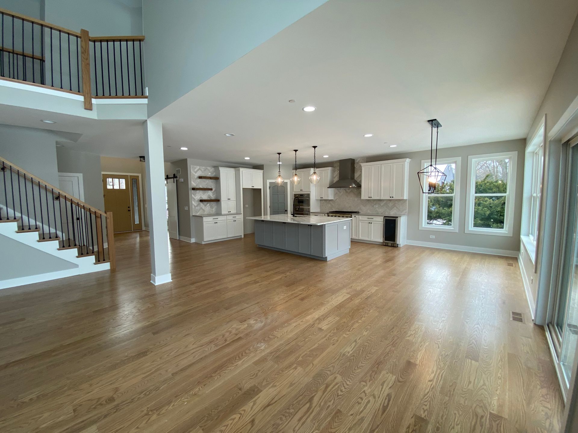 A large empty room with hardwood floors and a kitchen.