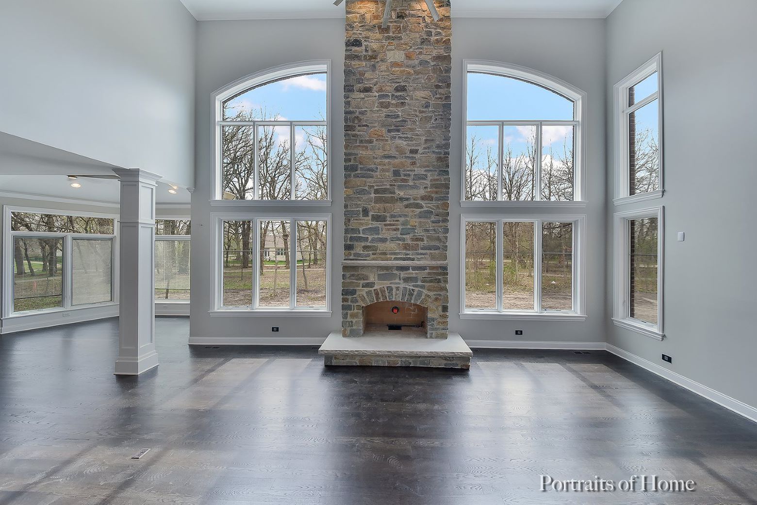 An empty living room with a stone fireplace and lots of windows.