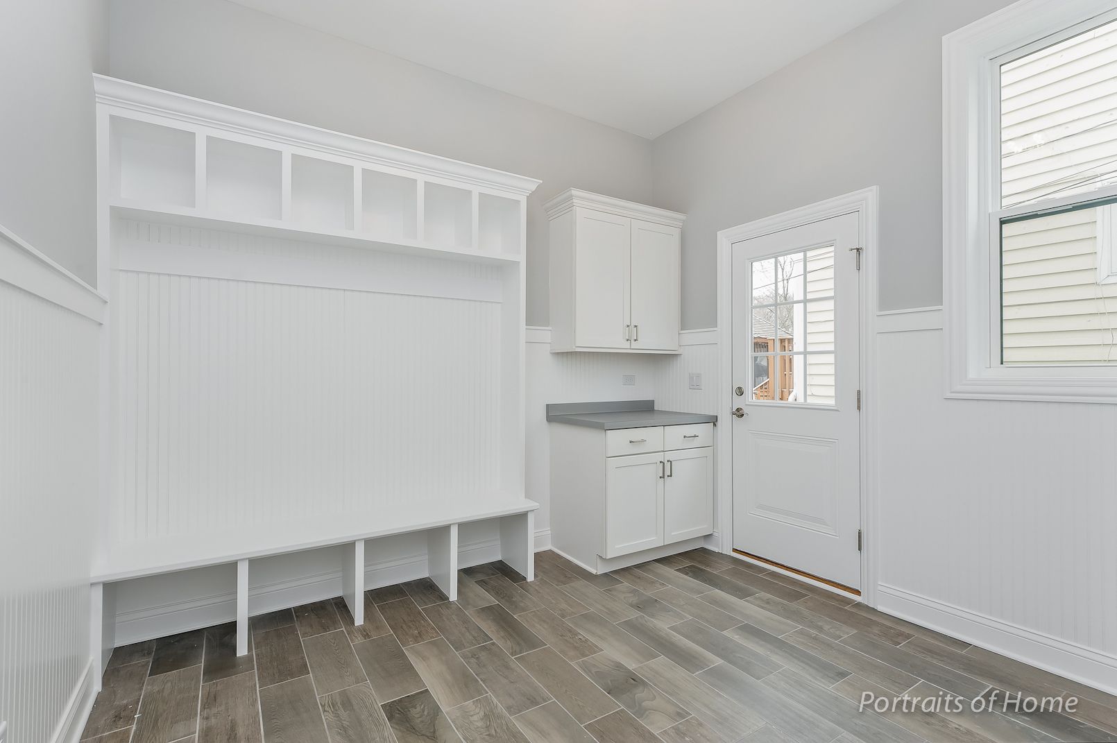 A room with hardwood floors , white cabinets , and a door.