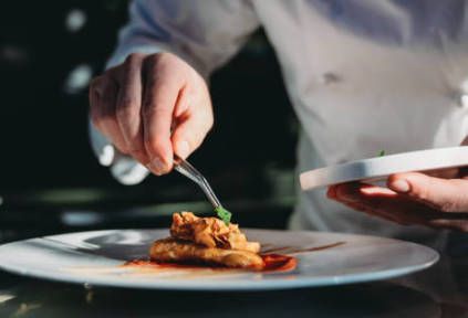 A chef is preparing a plate of food with a fork.