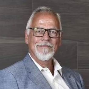 A man with a beard and glasses is wearing a suit and white shirt.