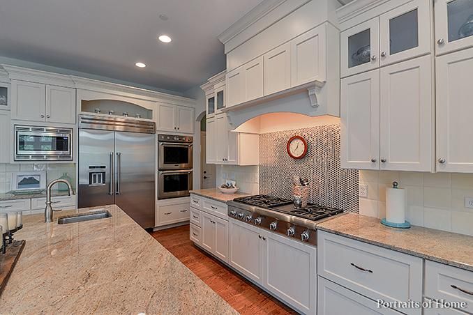 A kitchen with white cabinets , granite counter tops , stainless steel appliances and a large island.