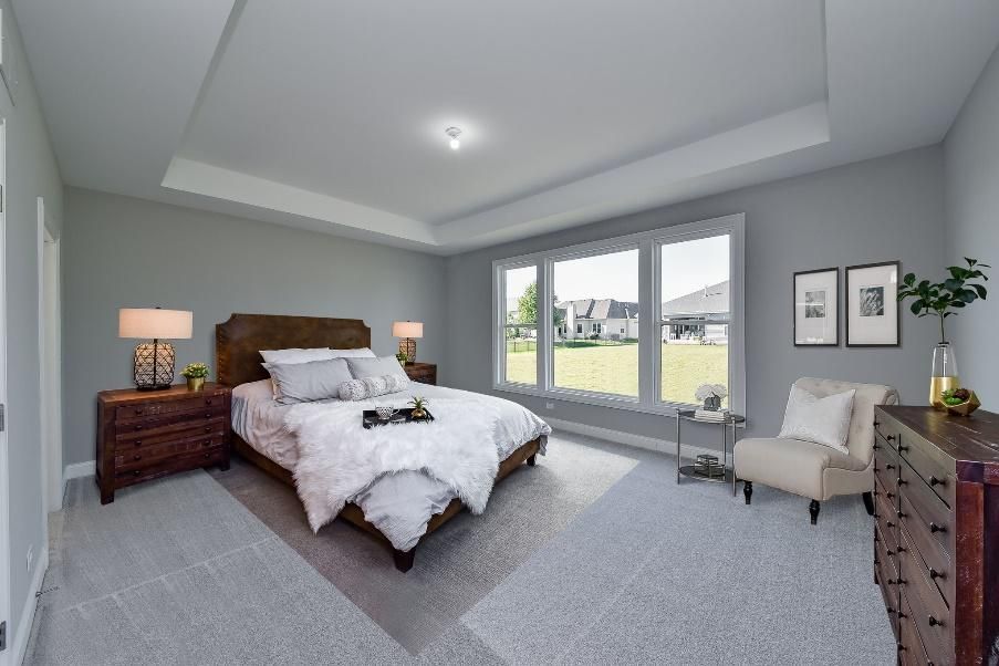 A bedroom with a bed , chair , dresser and windows.