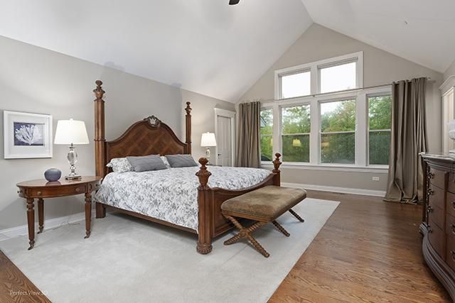 A bedroom with a king size bed , dresser , lamps and a bench.