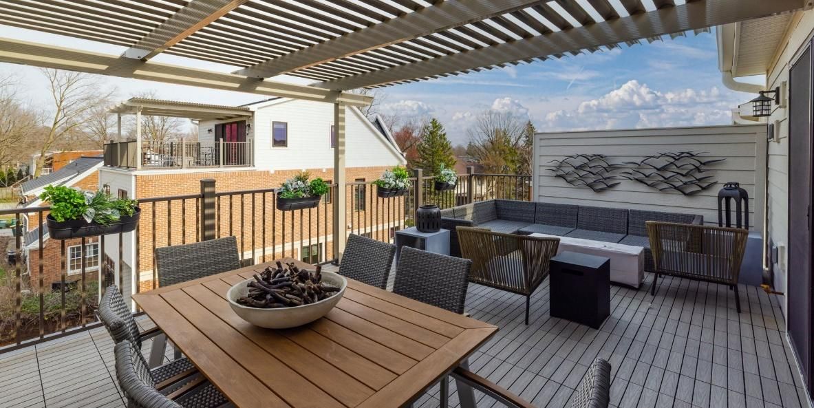 There is a table and chairs on the deck with a pergola.
