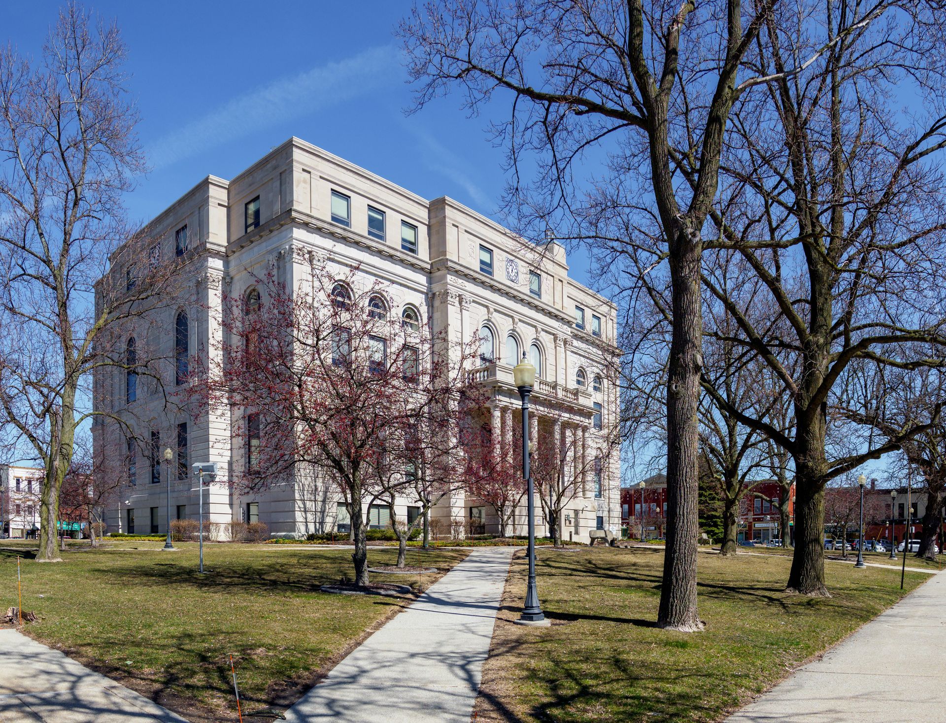 A large white building is surrounded by trees and grass on a sunny day.