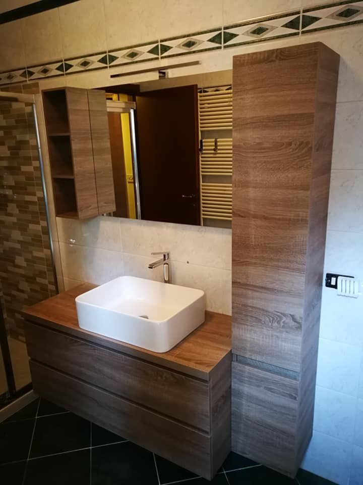 Un bagno con lavabo, specchio e mobiletti in legno.