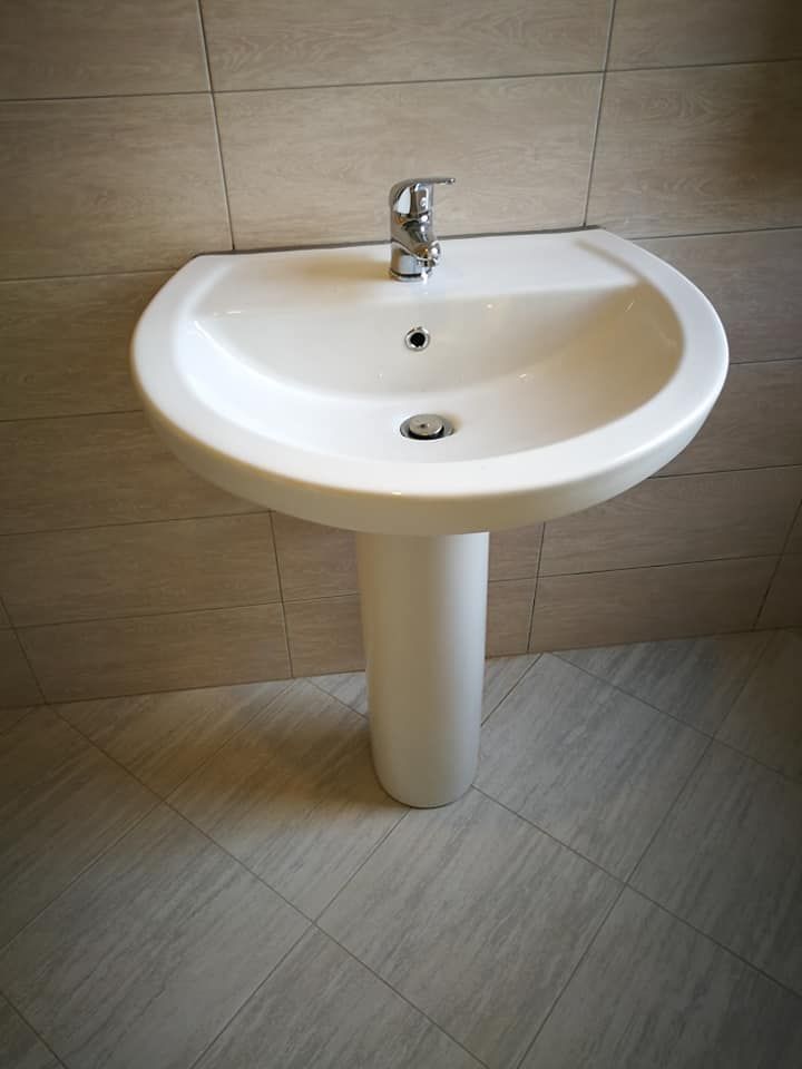 Un lavandino a piedistallo bianco con un rubinetto in un bagno.