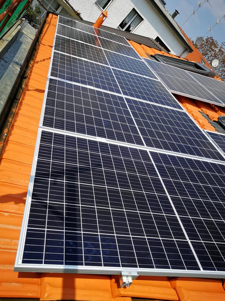 Una fila di pannelli solari è posizionata sopra un tetto di tegole arancioni.