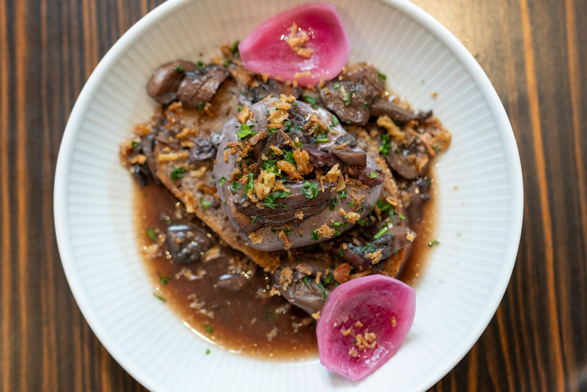 Plat composé d'une sauce foncée, de champignons et de radis marinés, servi dans un bol blanc.