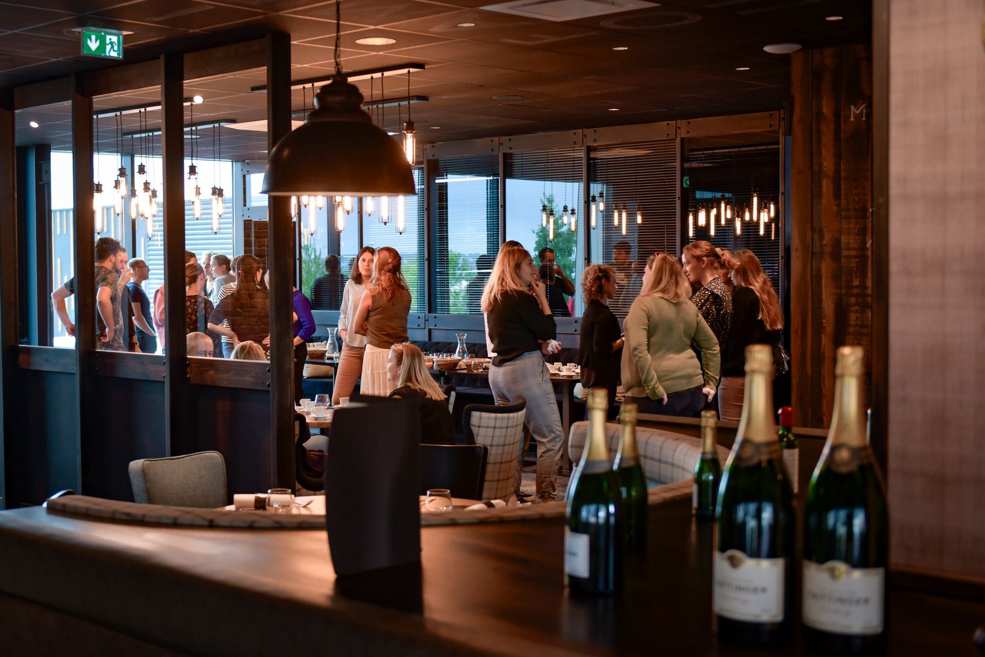 Intérieur d'un restaurant où des personnes discutent près d'un bar avec des bouteilles de champagne.