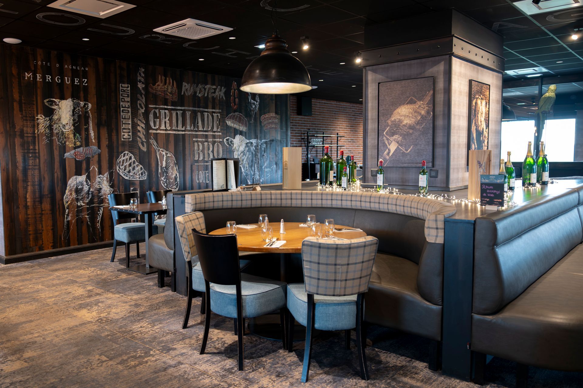 Intérieur du restaurant avec banquettes, tables et un coin bar aux murs sombres et à l'éclairage zénithal.