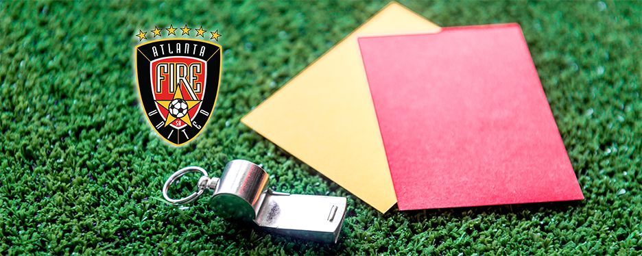 Soccer referee equipment on green turf. Red and yellow cards, whistle, and team logo.