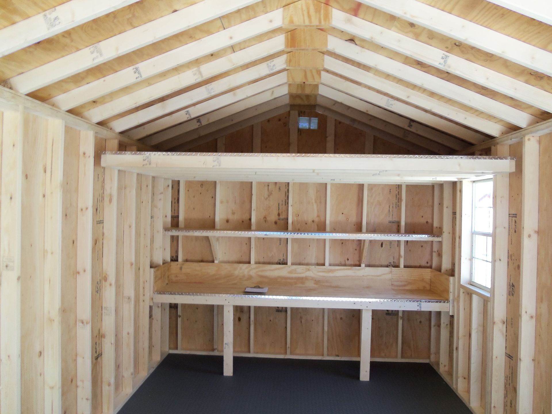 Wooden interior of a small shed with built-in shelves and a workbench under a sloped roof.