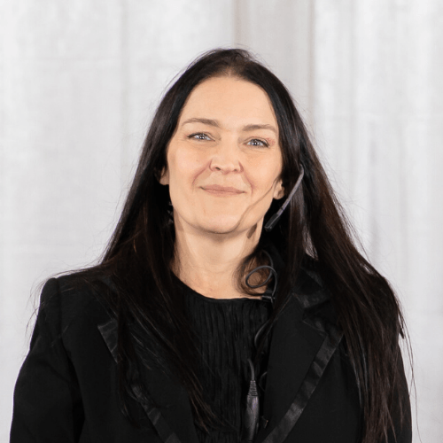 A woman wearing a headset and a black jacket is smiling.