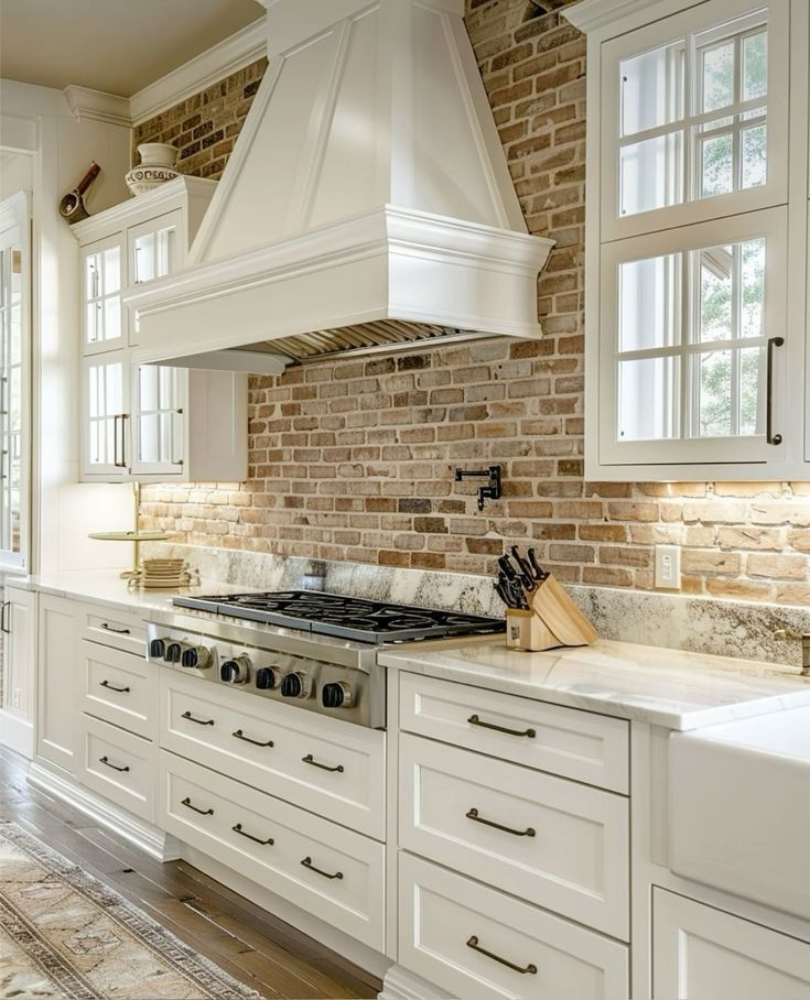 A kitchen with white cabinets , a stove , a sink and a brick wall.