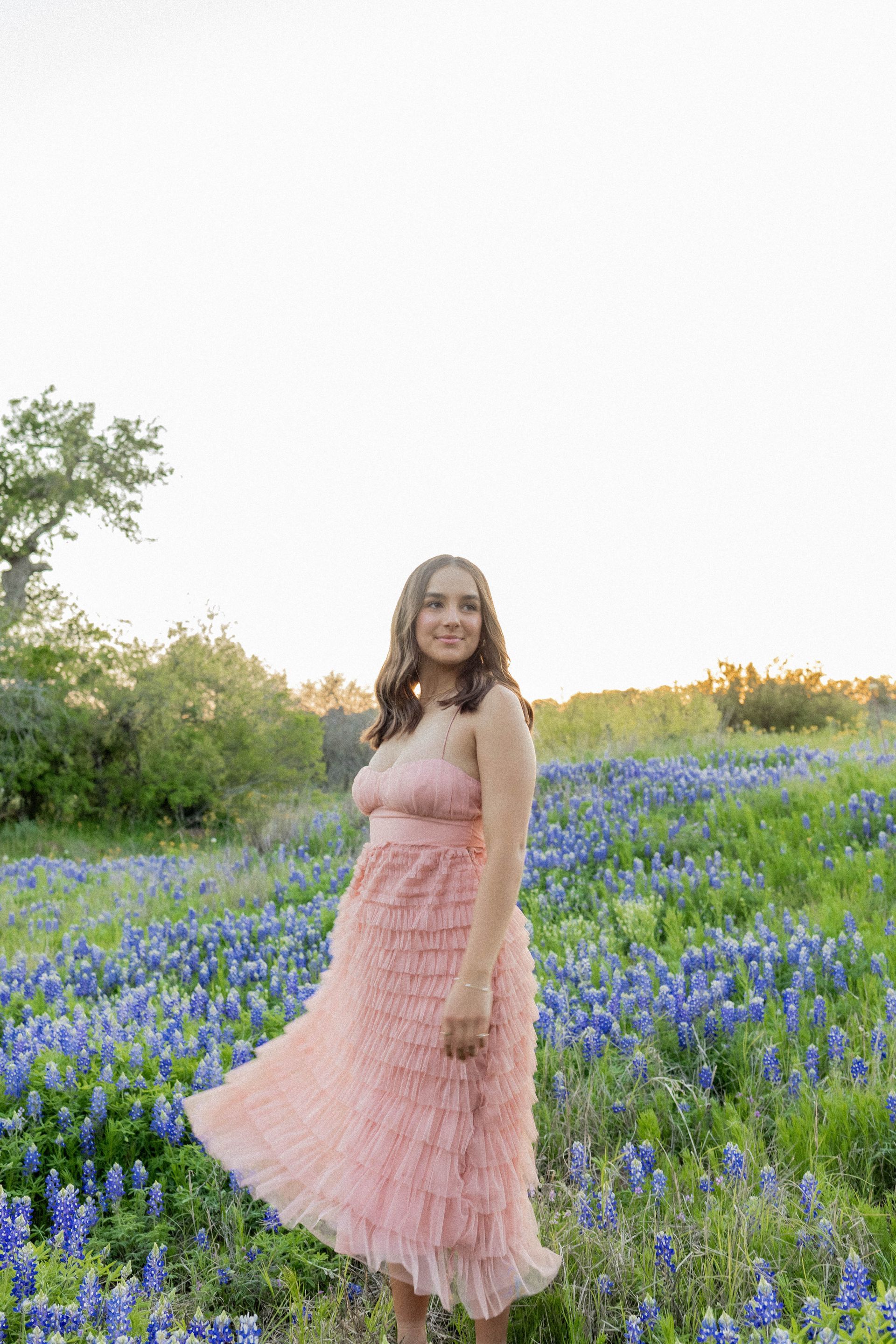 A woman in a pink dress is standing in a field of blue flowers.