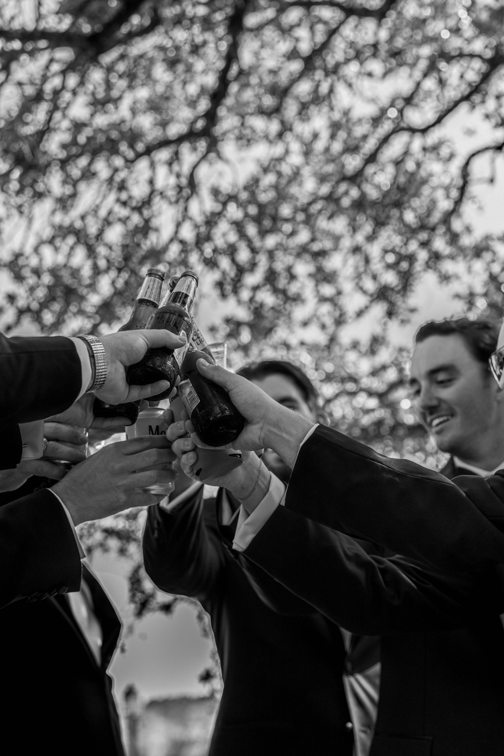 A group of men are toasting with beer bottles in a black and white photo.